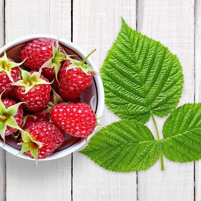 Raspberry with leaves on white wooden background
